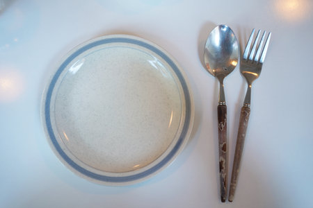 Empty plate with spoon and fork on white table. Top view.