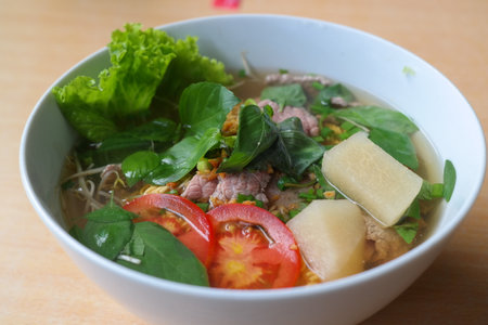 Thai noodle soup with pork and vegetables in white bowl.