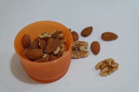Almond and walnut in orange bowl isolated on white background.