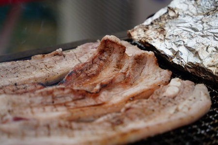 Close-up of pork belly being grilled on a charcoal grill.の写真素材