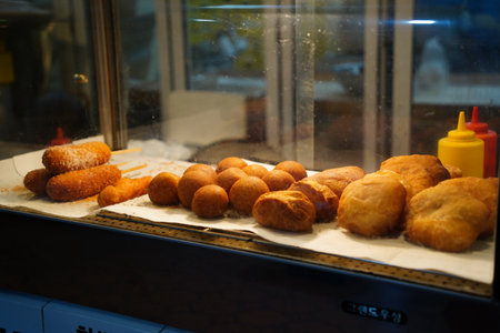 Assorted Korean Street Food Snacks, Including Corn Dogs, and Doughnuts, on Display in a Market Stall