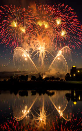 A colorful fireworks display is captured with multiple bursts taking place with their reflection in waterの写真素材
