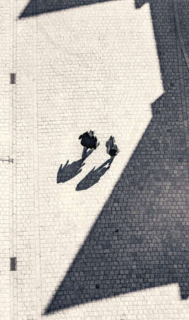Black and white image of two people walking down a cobble stone street taken from a high point of view and expressive shadowsの写真素材