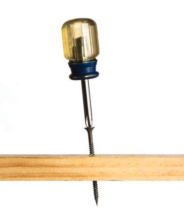 A screwdriver rests atop a large sharp screw in a piece of woodの写真素材