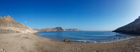 Panorama image of a beach or bay on the atlantic ocean with sand, grass, waves, high rocks and a blue sky with clouds on a sunny day in summerの写真素材