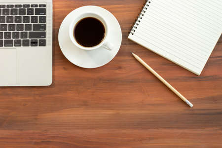 Coffee served in a cup, placed beside a portable computer. And have a pencil and notebook nearby