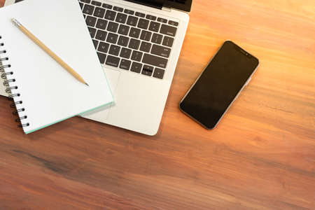 Coffee served in a cup, placed beside a portable computer and smartphone and have a pencil and note...