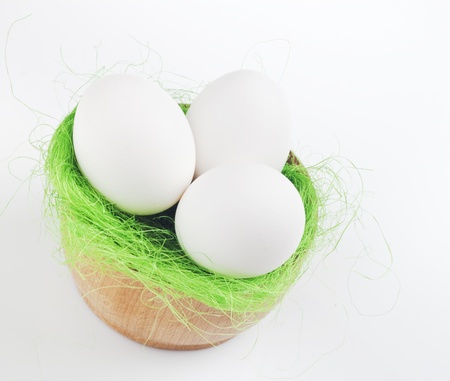 three eggs in a dish of artificial grass on a white background
