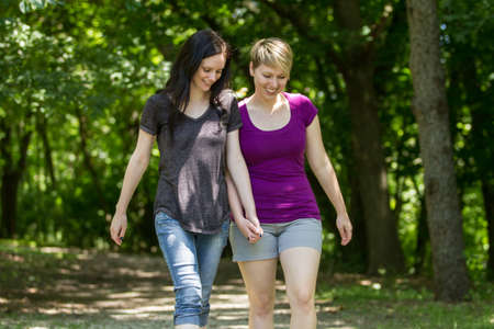 Girlfriends holding hands and walking in park, horizontalの写真素材