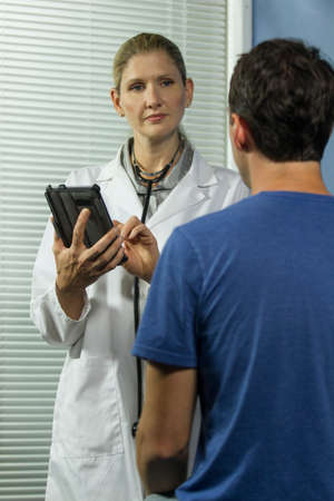 Female doctor holding tablet and listening to patient, verticalの写真素材