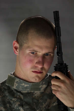 Sad soldier resting head on assault rifle, vertical