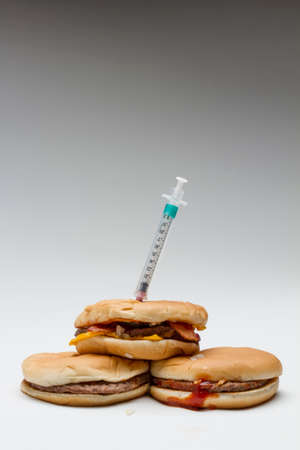 Syringe in fast food burgers, vertical