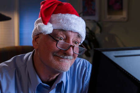Older man in Santa hat looks happy while reading off his computer monitorの写真素材