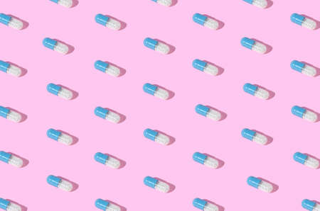 Creative pattern made with blue-white pills on pink background. Minimal sunlit layout.