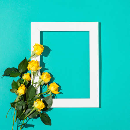Creative minimal concept made of yellow roses with green leaves and white frame on turquoise...