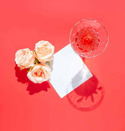 Roses and glass of juice on red background with blank paper card. Flat lay concept. Copy space.の写真素材