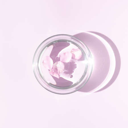 Floating soft pink rose petals in aromatherapy bowl with water. Top view minimal concept. Sun and shadows. Pastel background.の写真素材
