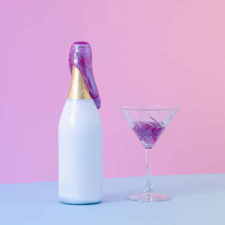 Party bottle of champagne with purple slime coming out of it beside crystal glass filled with slime. Blue table against pink wall. Creative minimal concept with purple gradient light.の写真素材