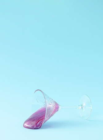 Purple glitter slime spilled out from crystal champagne glass on pastel blue background. Minimal party composition.の写真素材