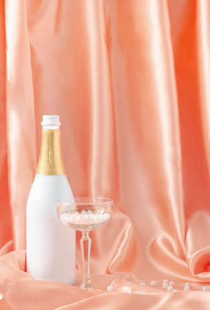 Smooth luxury design made with silk or satin curtain, bottle of champagne and crystal glass filled with white pearls. Minimal composition.の写真素材