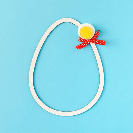 2021 Easter unique composition made of white egg frame, peace of boiled egg and red ribbon. Minimal holiday concept on pastel blue background. Flat lay.の写真素材