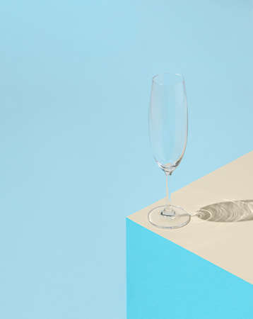 Empty champagne glass on pastel blue and beige background with sunny day shadow. Minimal abstract concept.の写真素材