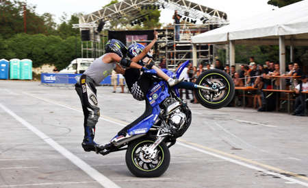 Stunt biker standing and girl sitting on handlebar, all on back wheel
