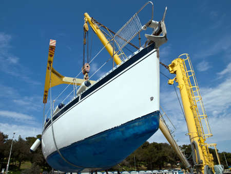 sailboat hanging on crane in harbor serviceの写真素材
