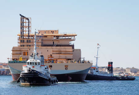 PULA, CROATIA - MARCH 7, 2015: Two tugboats tug special new ship "Isaac Newton". This is the first ship launch in 2015. in shipyard "Uljanik" Pula, Croatiaのeditorial素材