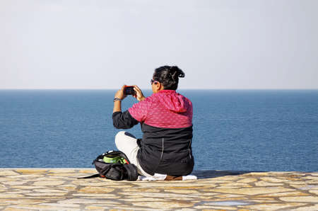 woman sitting on coastline and make photographの写真素材