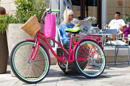 ROVINJ, CROATIA - SEPTEMBER 9, 2017: Unidentified woman reading and relaxing in bar after bicycle shopping in Rovinj, Croatia.のeditorial素材