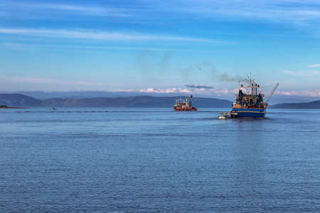 two fishing trawlers leave the port in early eveningの写真素材