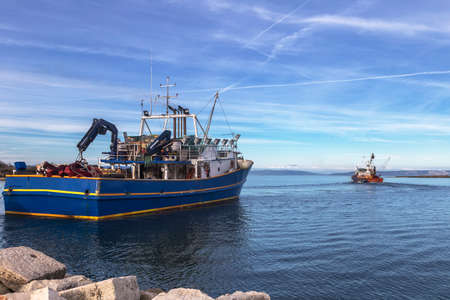 two fishing trawlers leave the port in early eveningの写真素材