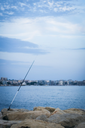 Fishing rod fixed on a stone coast in the front of a bay at Golfe Juan, Cote d'Azurの写真素材