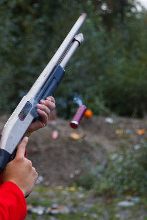 Close up of man holding a shotgun while ejecting the shell from the magazine. The shell is still hot and you can see it smoking as it flies outの写真素材