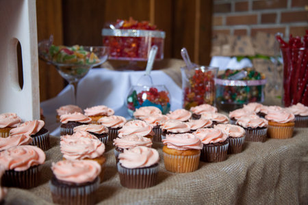 Pink frosted vanilla and chocolate cupcakes sit on a table cloth of burlap with other candies in the background as a dessert table for a wedding.の写真素材
