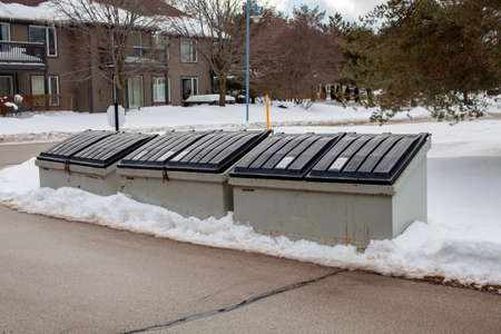 Three large metal garbage bin sits on the side of a street in a condo corporation for residents to...