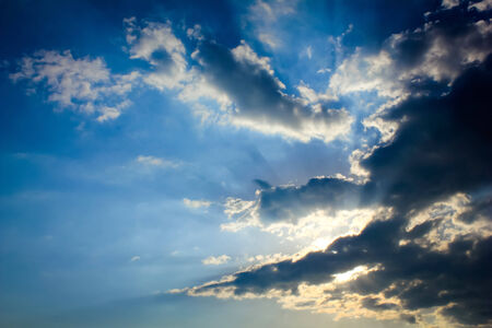 Bright sun rays through the dark clouds with deep blue sky background, creating beautiful scenery の写真素材