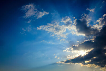 Bright sun rays through the dark clouds with deep blue sky background, creating beautiful scenery の写真素材