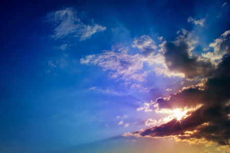 Bright sun rays through the dark clouds with deep blue sky background, creating beautiful scenery.の写真素材