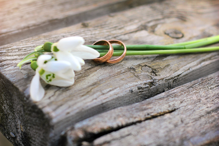 Two wedding rings and flowers of snowdrops on a wooden rustic background. Spring.の写真素材