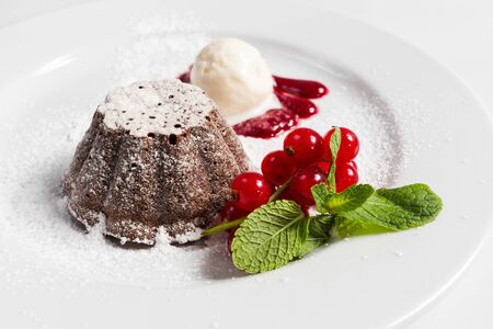 Plate of muffin with a sprig of red currant ice cream with red jam and mint sprinkled with powdered sugar. Chocolate cake with ice cream, berries and mint.の写真素材