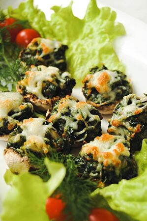 Stuffed mushrooms, stuffed with spinach, garlic and cheese Spinach and cheese mushrooms broccoli cheese with tomato in salad leaves and dill. tasty snack delicacy Greens under melted cheese mushrooms.の写真素材