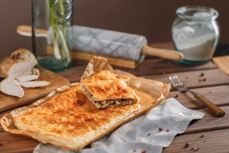 A square piece of meat pie on a rectangular meat pie on a wooden surface against the background of the ingredients from which it was made. Delicious meat pie on the table in cloth and meat in the background.の写真素材