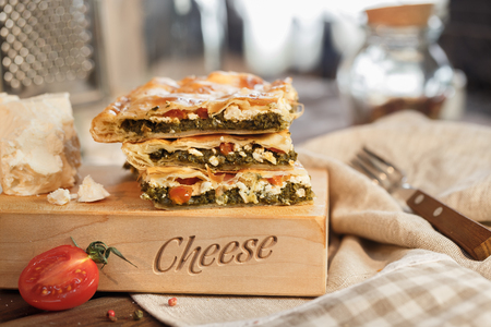 Vegetable pie with tomatoes spinach and herbs with cheese and delicious goat cheese with tomato and fork in the kitchen.の写真素材