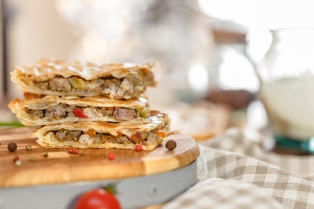 Appetizing meat baked pork cake with beef with potatoes and cheese and tomatoes and piece of pepper eat pie with appetizing pieces of meat with tomato pepper in peas on a wooden surface Puff pastry cake.の写真素材