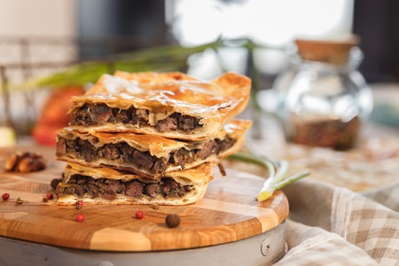 Pie with huge chicken liver pieces in juicy sauce with mouth-watering pieces of chicken meat with tomato pepper in peas on a wooden surface Puff pastry cake.の写真素材