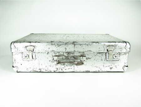 Vintage metal suitcase with a distressed silver finish, sturdy latches, and a central handle, showing signs of wear and age for a rustic, industrial aesthetic.の写真素材