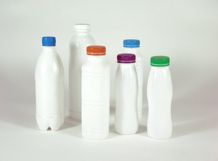 Six white plastic bottles with colorful screw caps (blue, orange, purple, green, and white) arranged in a group on a white background, representing beverage or dairy packaging.の写真素材