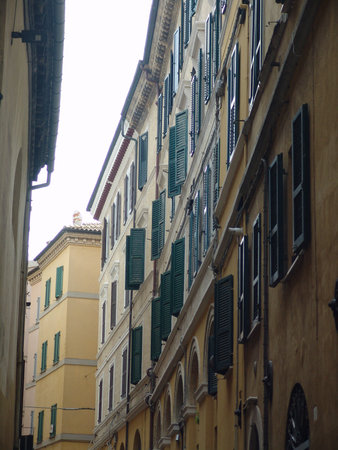 Narrow alley between historic buildings with tall facades, featuring multiple green wooden shutters on beige and yellow walls, creating a classic European architectural scene.の写真素材